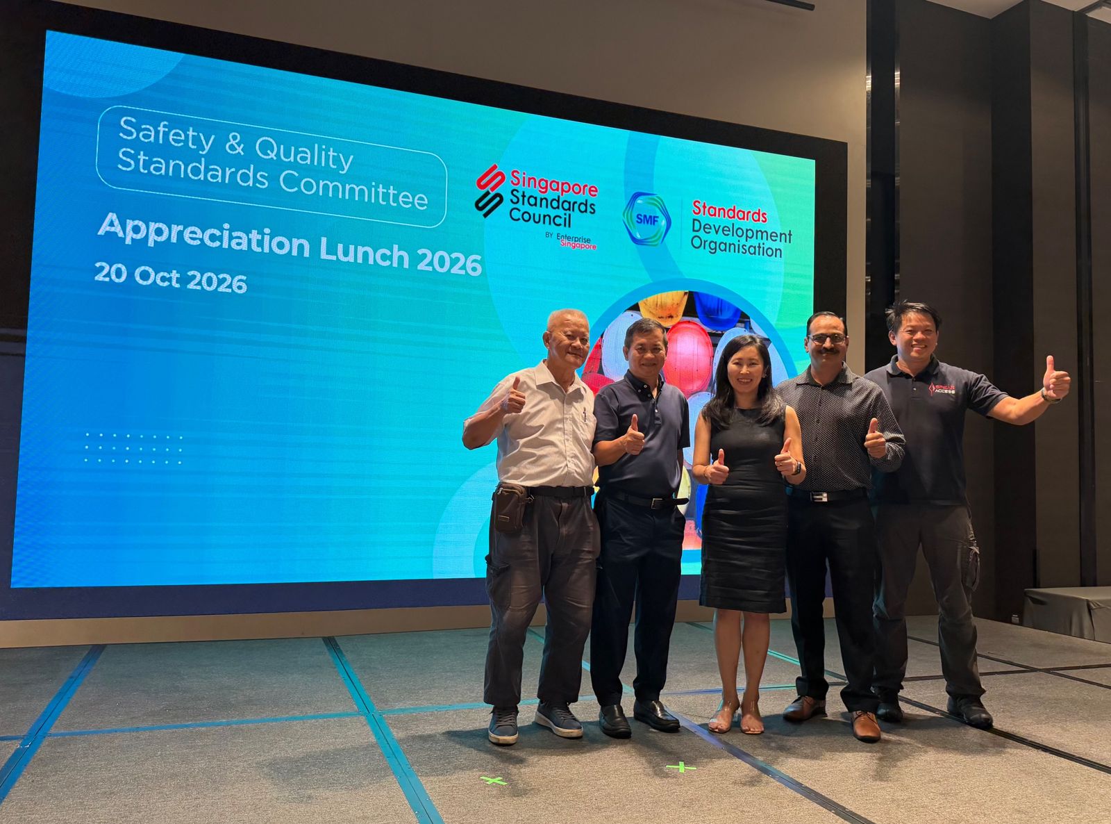 Five guests giving a thumbs-up in front of the Safety and Quality Standards Committee Appreciation Lunch 2026 screen